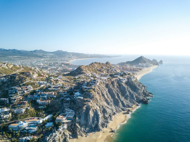 Aerial view of Cabo San Lucas, Mexico, featuring cliffside luxury homes, sandy beaches, and the famous Land’s End rock formations with the ocean in the background.